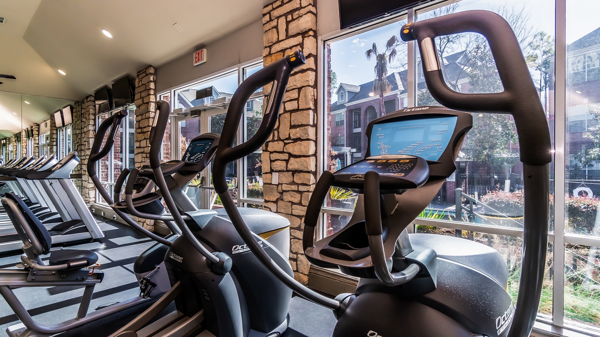 A row of treadmills in a gym with a view of the outside.